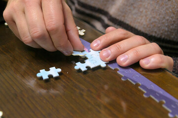 Close-up of the hands of a girl and her father doing a puzzle at the table in the living room. Authentic home hobbies concept.