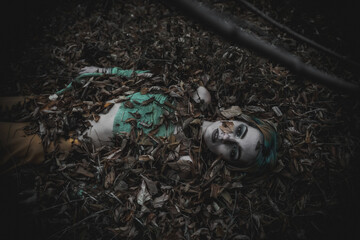 dead girl in autumn foliage wearing green and yellow robes