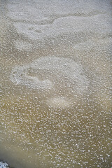 The frozen surface of the river. On the surface of yellowish ice there are large flakes of white snow and abstract patterns.