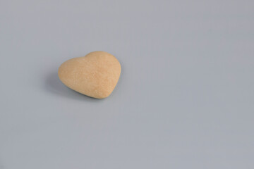 Obraz premium Single heart made of beige stone on gray background. Symbol of love, Valentine's Day concept. Close-up. Selective focus. Copy space.