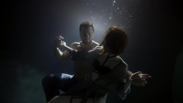 muscular man is holding graceful woman in hugs underwater, tenderness and love of young people