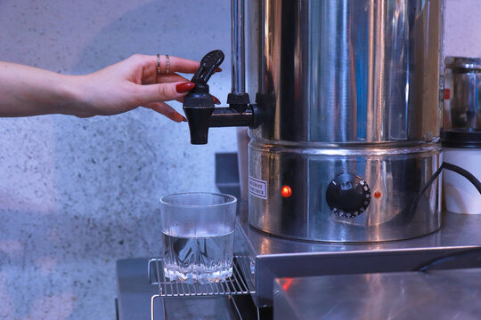 a woman's hand presses the tap to pour hot water from the boiler into a clear glass on the table