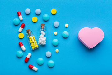 A lot of pills on blue background with a heart shape as a symbol of medical treatment for a healthy heart. Emergency help if a heart attack happened.