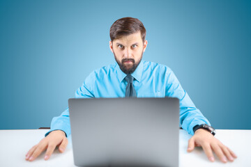 a businessman in a blue shirt and tie puts his hands on the table next to his laptop, and looks intently at the camera