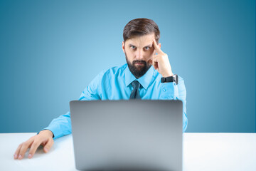 a businessman in a blue shirt and tie is working thoughtfully at a computer on a responsible project, the man leaned his hand to his head, thinking about work