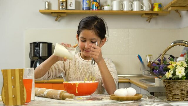 Kid girl preparing dough in orange bowl.  Concept of food preparation.   Homemade pastry. Preparing pasta or pizza. Eggs, rolling pin and flour on table.