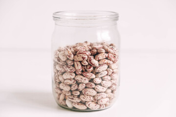 Raw beans in a glass jar on a white table background. Copy, empty space for text