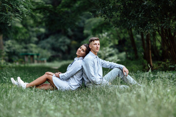 Outdoor shot of young happy couple in love sitting on grass on nature. Man and woman hugging, sunlight in summer park. Happy family in the evening sun light. The concept holiday.
