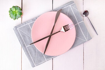 Close-up top view of serving empty pink plate with crossed knife and forks on folded linen napkin with geometric pattern. Selective focus. Mockup, copy space, minimalism.