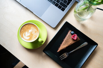 Cappuccino coffee chocolate cake and laptop working in a cafe