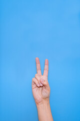 hand of a caucasian man doing victory symbol with fingers with blue background