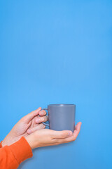 hands of a caucasian man wearing an orange jumper and holding a mug of coffee with blue background