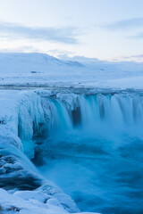 Scenic landscape view of tourist popular attraction Godafoss waterfall in northern Iceland in winter time. Long exposure falling water photo, snow covered mountains on background. 