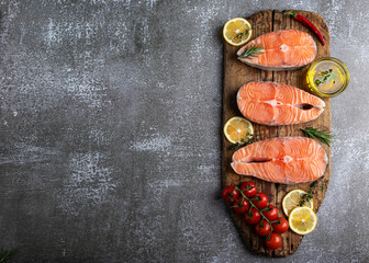 three raw steak fish trout, salmon and spices on wooden board, dark background, view from above