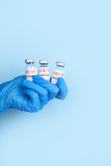 Vials of vaccination in the hand of a doctor with a glove on a blue background. Vaccine for COVID-19. Medicine infectious and money concept. Place for text