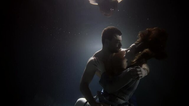 young loving couple is floating in darkness and depth of big aquarium or ocean, love and passion
