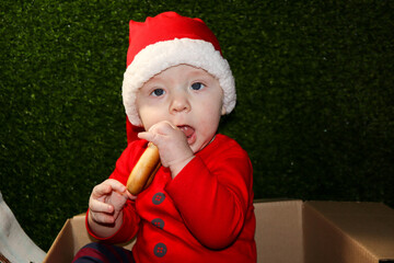 Fototapeta premium christmas gift - cute smiling child in red santa hat in the cardboard box eating the bagel