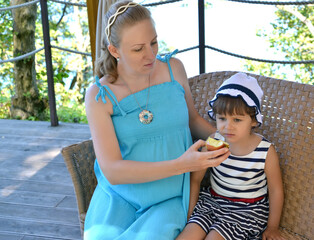 Mom feeds three-year-old daughter with an apple outdoors