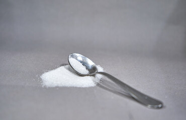 silver spoon on grey background with some sugar on it