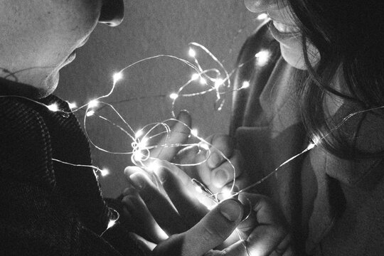 a guy and a girl are holding a garland of lights in their hands. hands with rings, wedding concept, grainy photography.