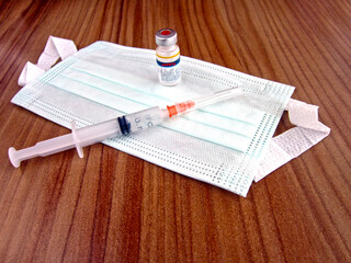 Surgical mask, vaccine and syringe on wooden table.