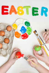 Handmade stuffed colorful felt letters and same color brush with paint on white background.Easter concept. Egg painting theme. Visible eggs, child hands and painting process.