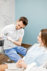Obraz premium Dentist showing a jaw prototype with teeth problems for a young patient for an orthodontic treatment. Girl having a consultation with a orthodontist. High quality photo