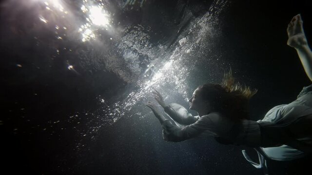 graceful young woman is swimming underwater, touching mirror surface of pool, subaquatic shot