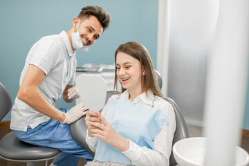 Young girl in dental braces looking on her beautiful teeth at the dental mirror during an orthodontic treatment, happy with the result. High quality photo