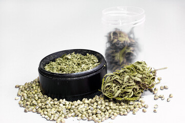 grinder full of dry herb and joint with medical marijuana with paper filter and piece of rolling paper on white background