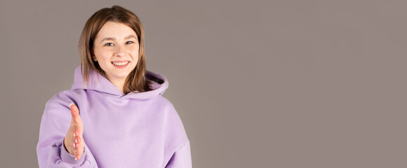 Young woman in purple sweater reaching for shake hand to greet someone, isolated on gray background.