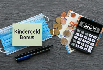 Notizblock mit dem Schriftzug Kindergeldbonus mit Taschenrechner,Geldscheinen und Mundschutz 