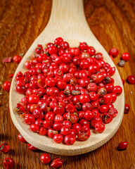 Schinus molle, schinus terebinthifolius. heap of rose pepper on a spoon and wooden board