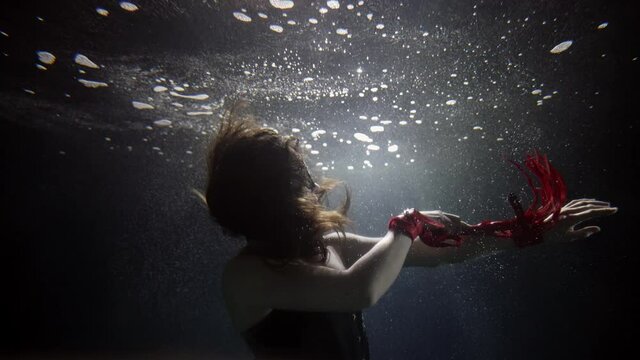 underwater shot of mistress with red whip, woman is playing with knout, stroking her body in water