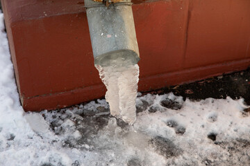 Frozen ice melts in icicles from the drainpipe of the house. The approach of spring in the city.