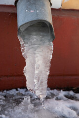 Frozen ice melts in icicles from the drainpipe of the house. The approach of spring in the city.