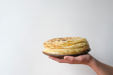 Stack of russian pancake blini in rustic wooden dish woman holds in hands on a grey background....