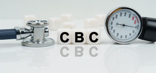 On a reflective white surface lies a stethoscope and cubes with the inscription - CBC