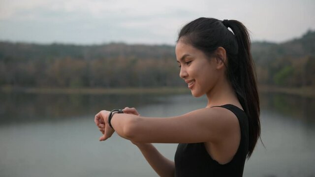 A young woman is using smartwatch while exercise in nature outdoor at sunset