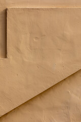 Vertical close-up image of a beige stucco wall, with a long, thin shelf at top and a triangular indent across bottom and lower right, a useful image for copy space.