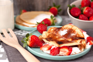 Vista en primer plano de un plato de crepes con nata y trozos de fresas.