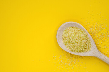 Couscous groats (made of durum hard wheat) in wooden spoon isolated on yellow background, top view