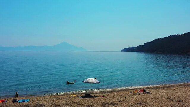 Drone flying over the beautiful Fava beach in Greece. There are a few people on the beach, and swimming in the blue ocean. There are mountains in the background. 4K