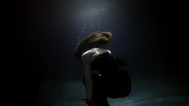 woman is sinking in dark pool, underwater shot, slow motion, dramatic mood