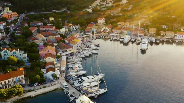 Drone flying over the beautiful marina and town of Fiskardo in Greece. There are a lot of boats in the marina. It is a beautiful evening around sunset, with sun flares in right side of frame. 