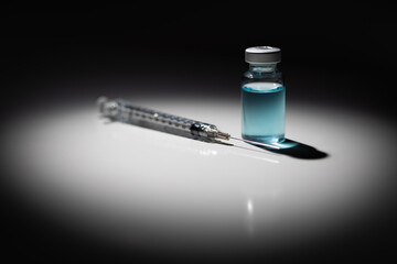 Syringe Needle and Medicine Vial With Light Blue Chemical Spot Lit on Reflective Background