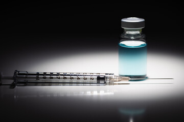 Syringe Needle and Medicine Vial With Light Blue Chemical Spot Lit on Reflective Background