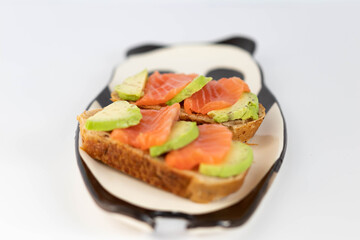 Homemade toast sandwich with salmon and avocado on a slice of cereal bread. The toast lies on a plate in the shape of a black and white panda. healthy food.