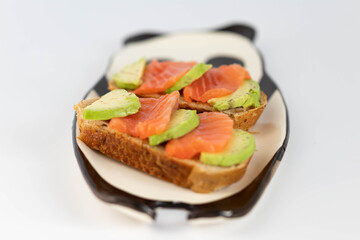 Homemade toast sandwich with salmon and avocado on a slice of cereal bread. The toast lies on a plate in the shape of a black and white panda. healthy food.