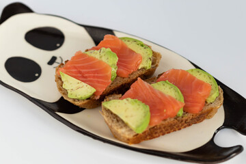 Homemade toast sandwich with salmon and avocado on a slice of cereal bread. The toast lies on a plate in the shape of a black and white panda. healthy food.